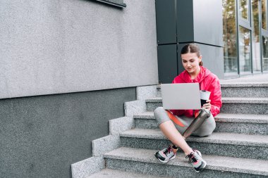 Sokakta merdivenlerde otururken dizüstü bilgisayar kullanan engelli sporcu kadın