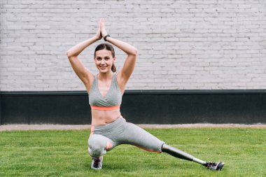 Gülümseyen engelli kadın protezle çimenlerde yoga yapıyor.