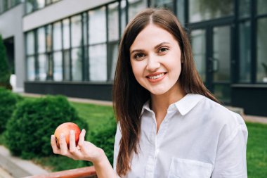 smiling attractive young woman holding apple on street clipart