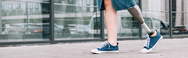 панорамный снимок женщины-инвалида в джинсовой юбке идущей по улице
