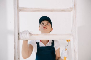 Üniformalı genç bir ressam merdivene tırmanırken yukarı bakıyor.
