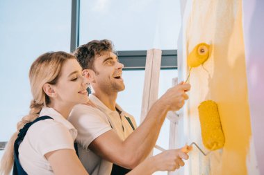 İki genç ressam duvarları boya rulolarıyla boyarken gülümsüyor