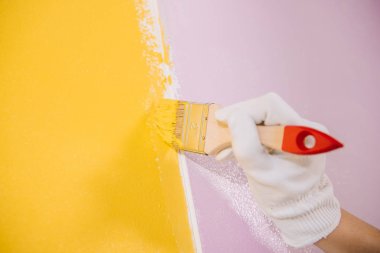 Boyacının sarı ve pembe boya fırçasıyla duvar boyamasının kısmi görüntüsü