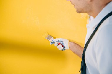 Duvarı boya fırçasıyla sarıya boyayan genç ressamın kırpılmış görüntüsü