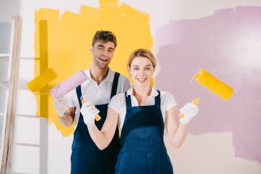 two young painters smiling at camera while holding paint rollers clipart