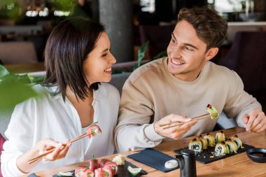 Lokantada ellerinde lezzetli suşiyle yemek çubukları tutan mutlu adam ve neşeli kadın. 