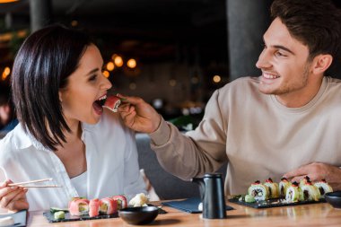 Lokantada genç bir kadının yanında lezzetli suşiyle yemek çubuğu tutan mutlu adamın seçici odağı. 