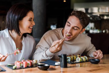 Suşi barda mutlu bir kadının yanında yemek yerken yemek çubuğu tutan adamın seçici odağı.