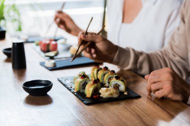 Sushi dürümlerinin yanında çubuk tutan bir adam ve bir kadın. 