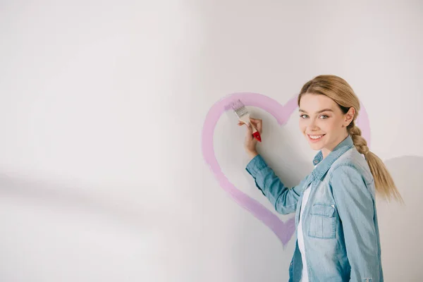 Szczęśliwa Młoda Kobieta Malowanie Różowe Serce Pędzlem Białej Ścianie — Zdjęcie stockowe
