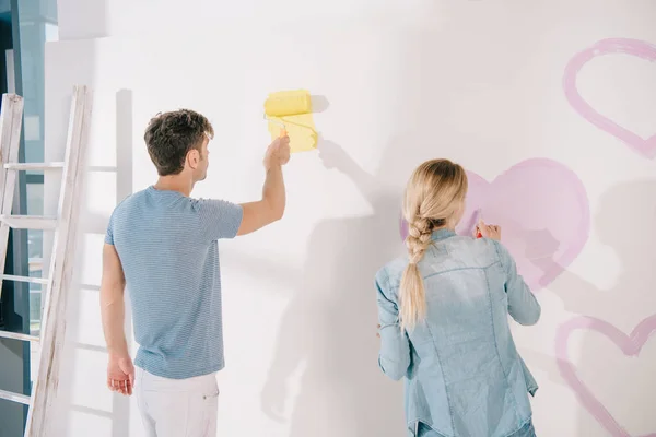 男人用黄色粉刷白墙 而女朋友则用粉色心来画 — 图库照片