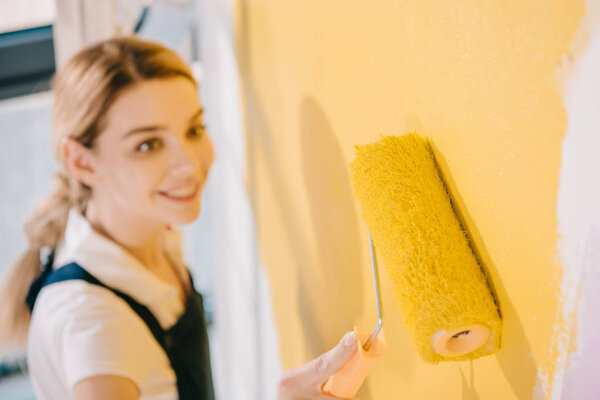 selective focus of young painter painting wall in yellow with paint roller