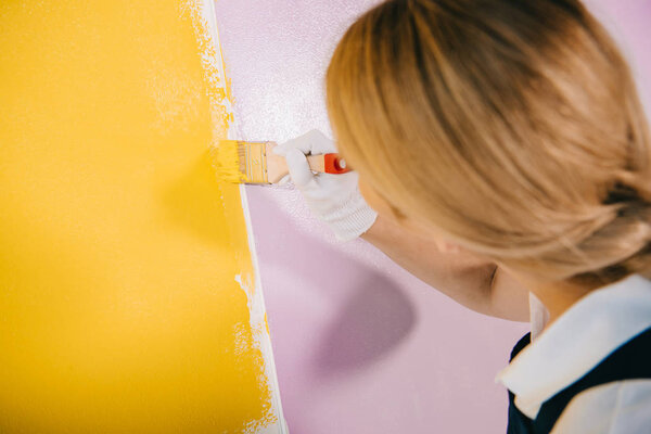 back view of young painter painting wall in yellow and pink with paintbrush