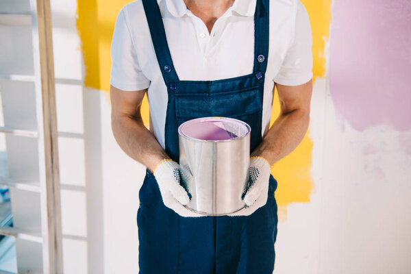 cropped view of painter in uniform holding can with paint