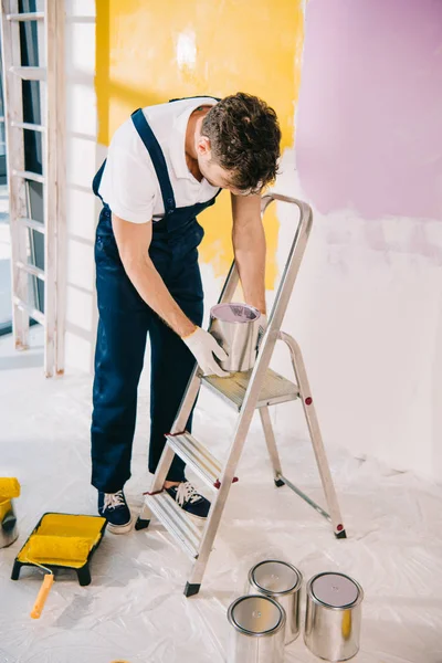 身穿制服的年轻画家站在梯子旁边 开着的罐子上涂着油漆 — 图库照片