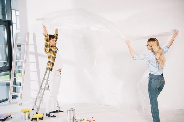 Pareja Joven Sosteniendo Celofán Mientras Prepara Para Pintura Pared — Foto de Stock