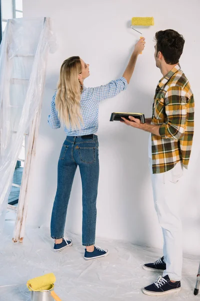 Joven Mujer Pintura Pared Amarillo Mientras Novio Celebración Bandeja Rodillos — Foto de Stock