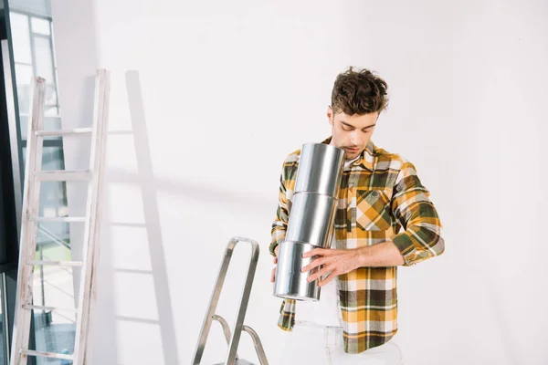 Joven Guapo Sosteniendo Latas Con Pintura Mientras Está Pie Cerca —  Fotos de Stock