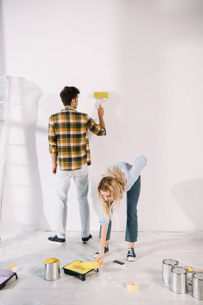 молодая женщина положить краску ролика в лоток с желтой краской, а парень картина стены
