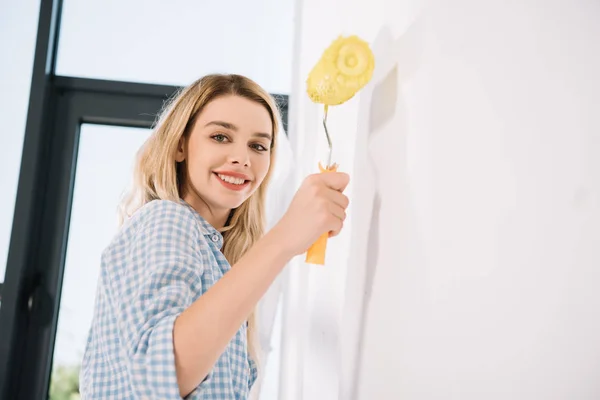 Alegre Joven Mujer Sosteniendo Amarillo Pintura Rodillo Mientras Pie Cerca — Foto de Stock
