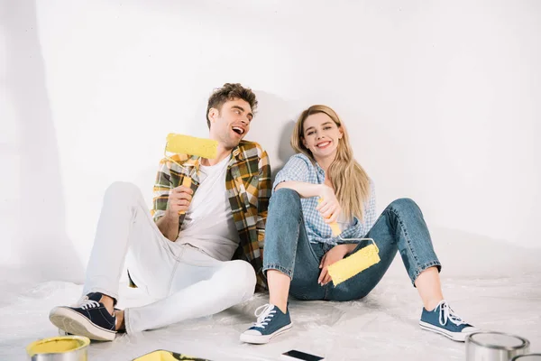 Happy Young Couple Sitting White Wall Holding Yellow Paint Rollers — Stock Photo, Image