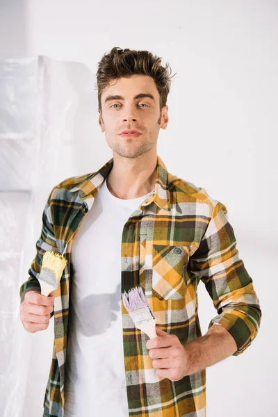 Handsome Young Man Looking Camera While Holding Yellow Pink Paintbrushes — Stock Photo, Image