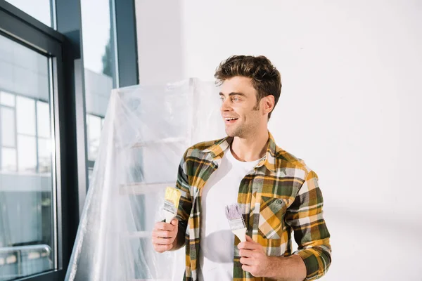 Handsome Young Man Looking Away While Holding Yellow Pink Paintbrushes — Stock Photo, Image