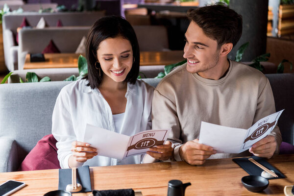 handsome man looking at happy woman smiling holding menu
 
