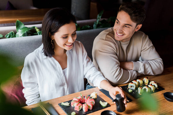 selective focus of happy man looking at cheerful woman smiling near plates with sushi 