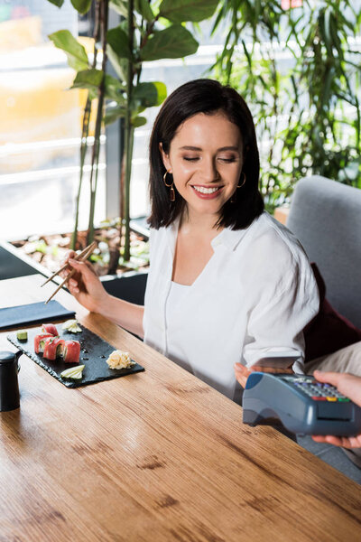 cropped view of waiter holding credit card reader near woman paying with smartphone 