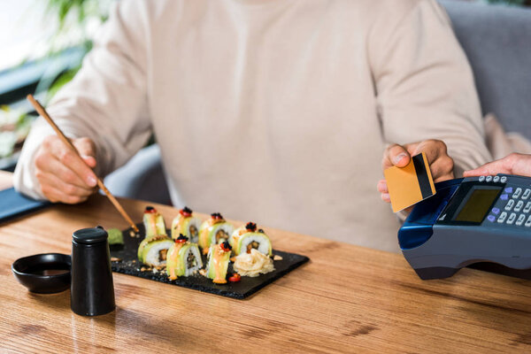 cropped view of waitress holding payment terminal near man with credit card