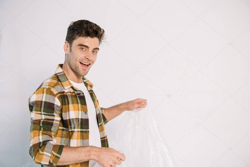smiling young man holding cellophane while preparing for wall painting