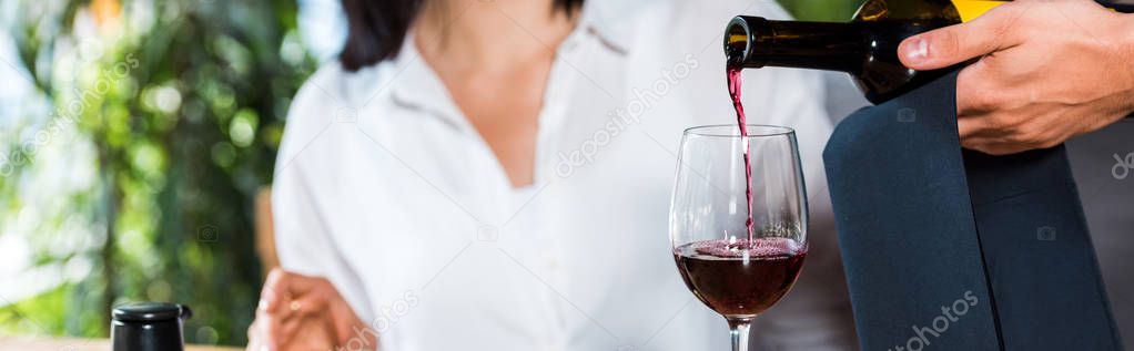 panoramic shot of waiter pouring red wine in glass near woman 