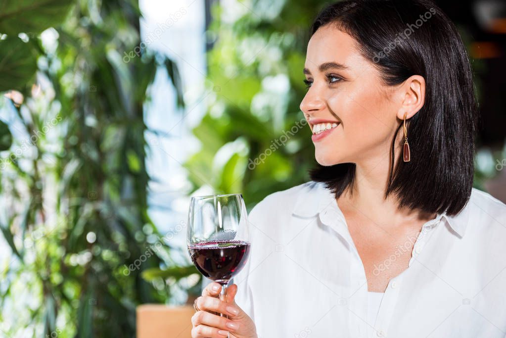 happy young woman holding glass with red wine in restaurant 