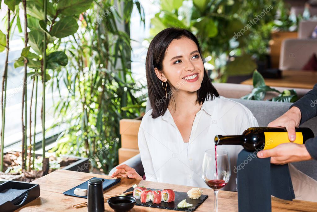 cropped view of waiter pouring red wine in glass near attractive woman 