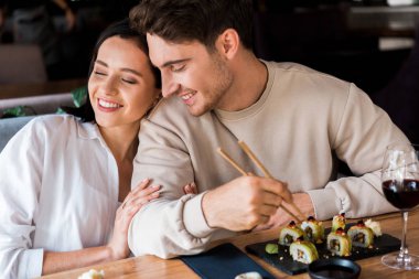 Sushi 'nin yanında yemek çubuğu tutan mutlu bir adam. Gözleri kapalı çekici bir kadının yanında.