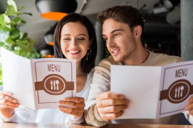 selective focus of man and happy woman looking at menus in restaurant  clipart