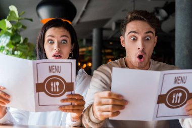 shocked man and woman looking at menus in restaurant  clipart