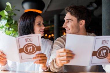 happy man and woman looking at each other while holding menus in restaurant  clipart