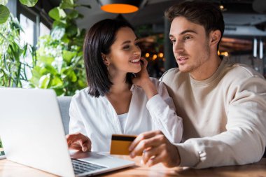 Seçici odak noktası, mutlu bir kadının dizüstü bilgisayarın yanında kredi kartı olan bir adama bakması. 