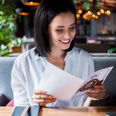 selective focus of cheerful woman sitting in sushi bar and looking at menu  clipart