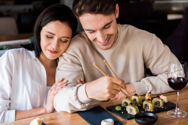 happy man holding chopsticks near sushi near attractive woman 