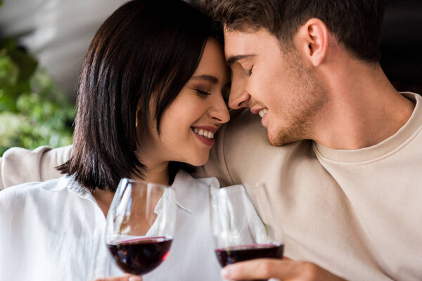 happy man and cheerful woman with closed eyes holding glasses with red wine 