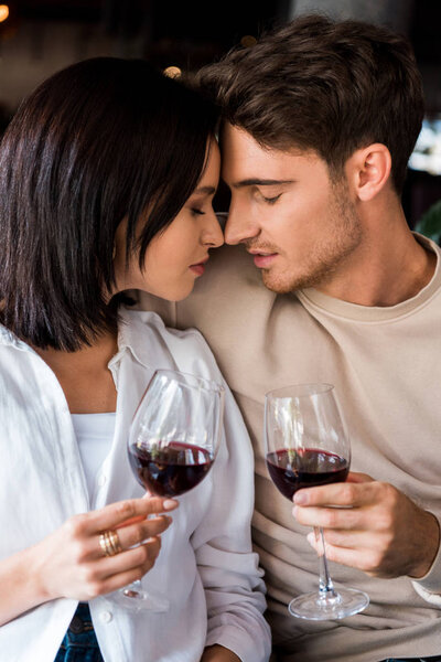 man and woman with closed eyes holding glasses with red wine 
