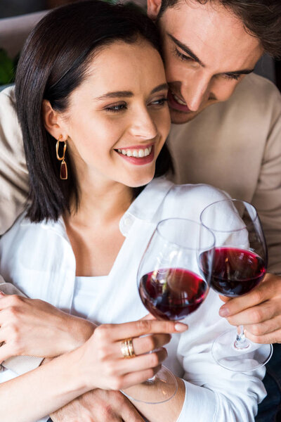 happy man holding glass with wine near cheerful girl 