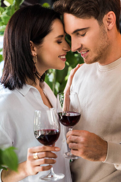 selective focus of happy man holding glass with red wine near beautiful girl 
