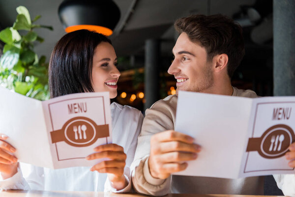 happy man and woman looking at each other while holding menus in restaurant 
