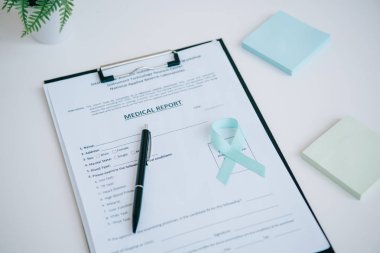 blue awareness ribbon on medical report near pen and sticky notes clipart