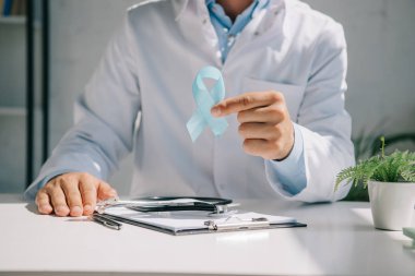 cropped view of doctor sitting at desk and showing blue awareness ribbon clipart