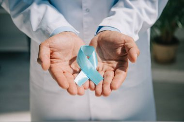 Mavi farkındalık kurdelesi taşıyan beyaz önlüklü bir doktor.